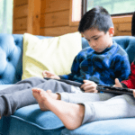 two boys on the sofa in a cabin playing on their tablets