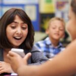 Girl showing friend her phone in classroom