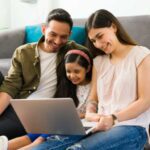 Parents and child sitting on floor with laptop, smiling together