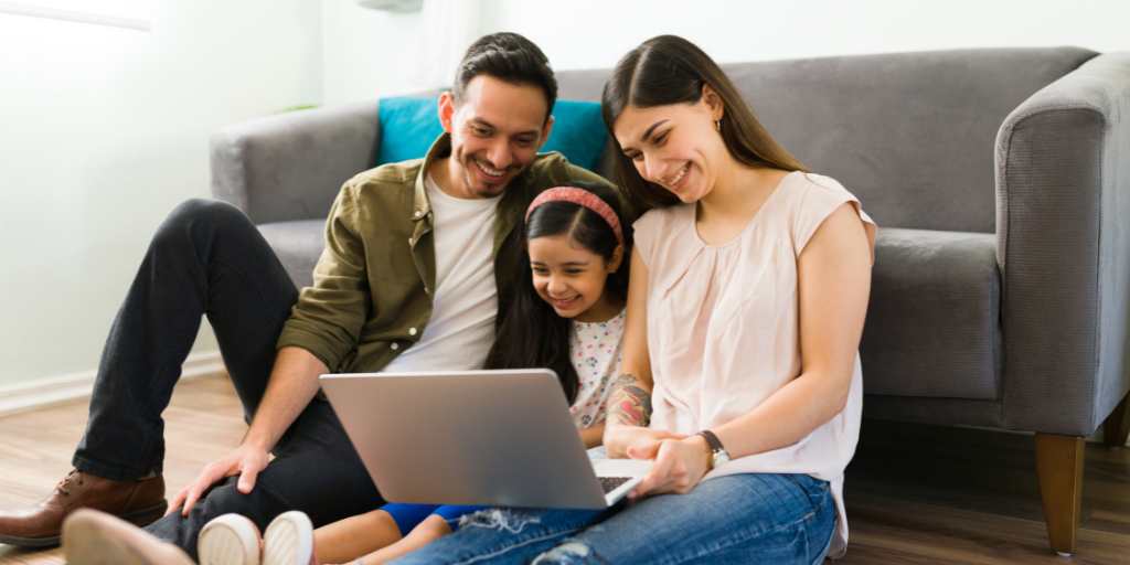 Parents and child sitting on floor with laptop, smiling together