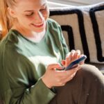 Woman smiling at phone while sitting on couch