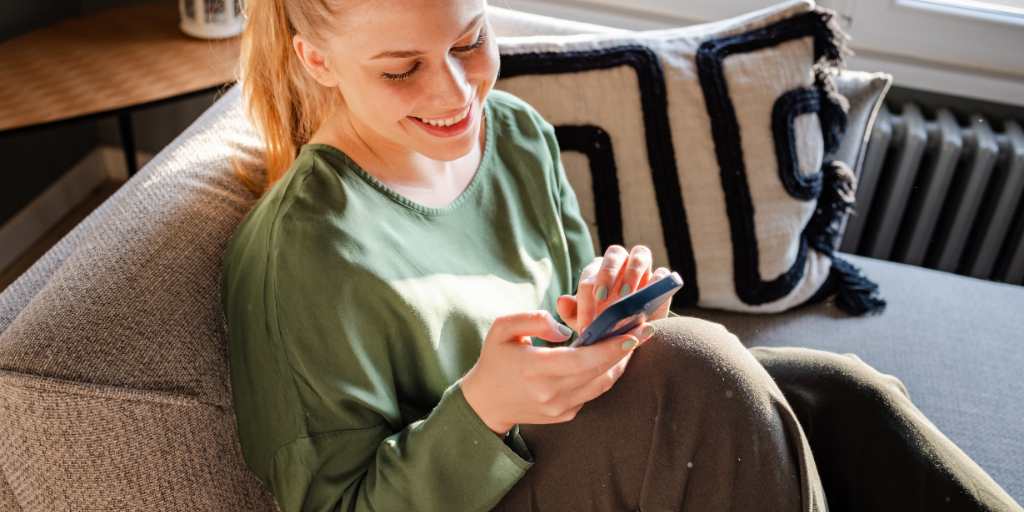 Woman smiling at phone while sitting on couch