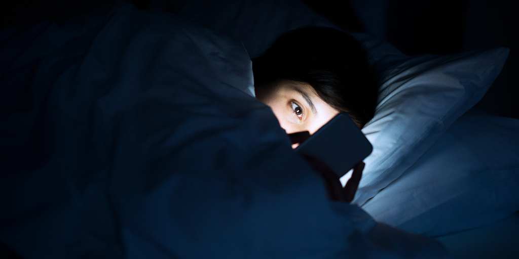 child looking at phone in bed