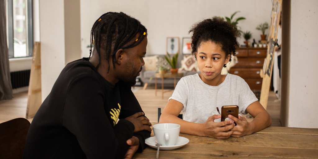 daughter looking at dad at kitchen table while holding phone