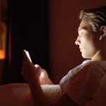 teen boy looking at phone in bed