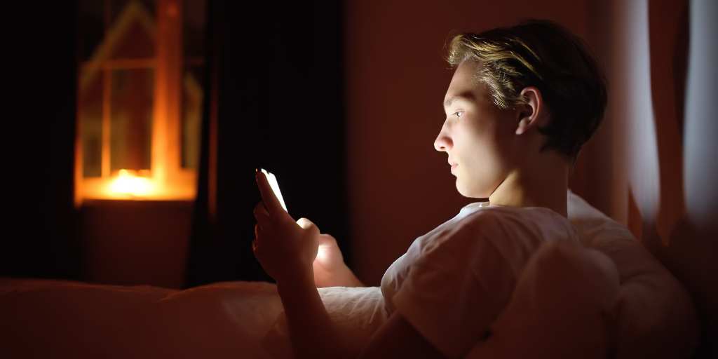 teen boy looking at phone in bed