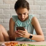 teen looking at social media while eating meal at table