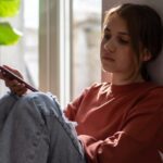 stressed teen leaning against wall and looking at phone
