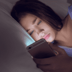 Teen looking at phone on bed in dark